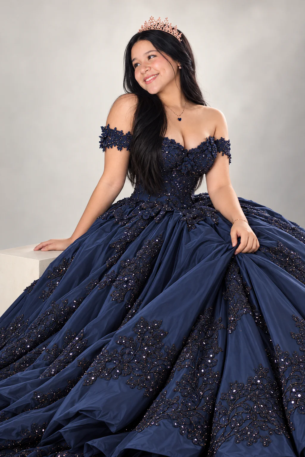 Valery sentada con vestido azul marino, sonriendo mientras mira fuera de cámara